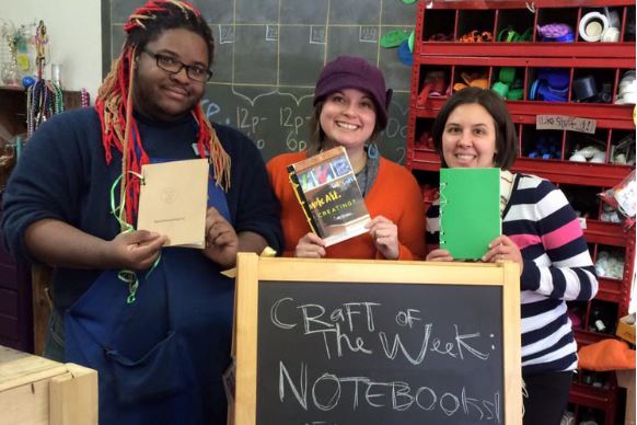 Crafters holding up notebooks made at an Upcycle Parts shop event.