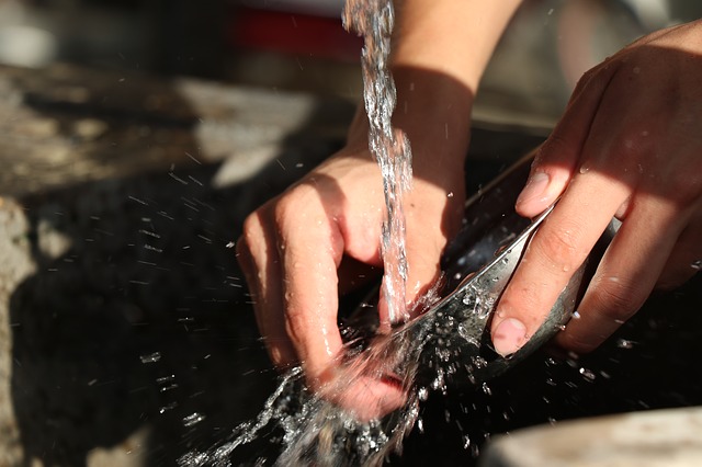 Hands washing a dish under running water.
