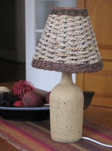 Reusing a glass bottle by turning it into a lamp with a taupe finish and basket-style shade.