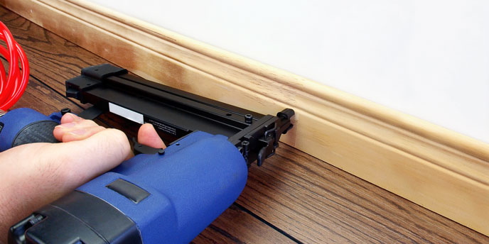 Carpenter Using Nail Gun on Baseboard