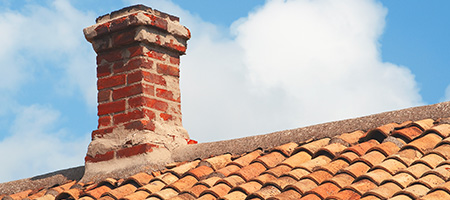 Brick Chimney on Terracotta Roof in Front of Partly Cloudy Skies
