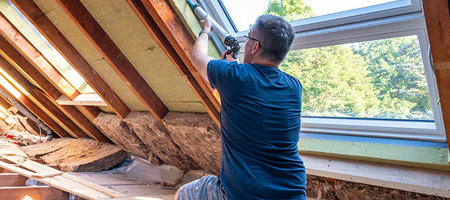 Person Caulking Air Leaks in Attic Near Window.