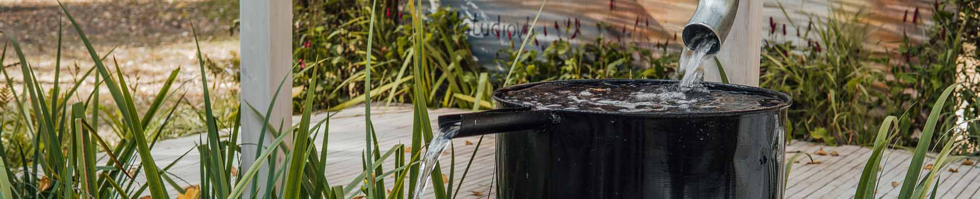 Water Flowing Into Black Rain Barrel Next to Plants