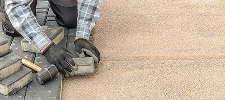 Person Installing Gray Concrete Pavers With a Mallet