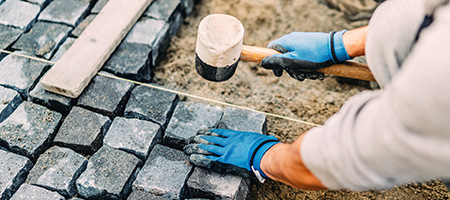 Person Installing Gray Belgian Blocks With a Mallet