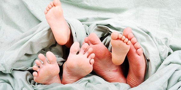 Family's Feet Underneath Sheets on a Bed