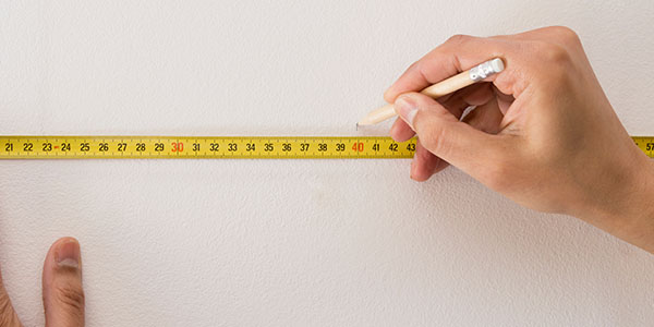 Hand Holding Measuring Tape to Measure Wall