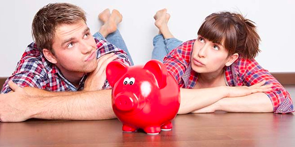 Couple Laying on Hardwood Floor Behind Red Piggybank