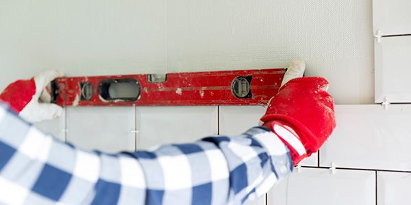 Man Uses Level and Spacers to Keep Tiles Lined Up