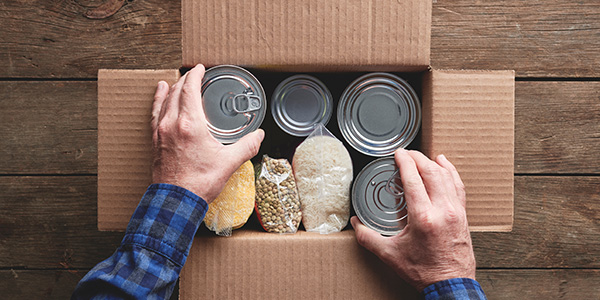 Person Placing Canned Goods in a Donation Box.