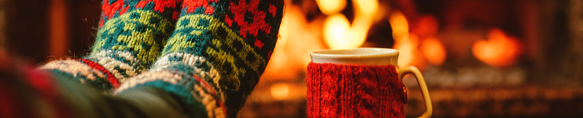 Coffee Cup and Feet in Winter Socks Sitting on Table in Front of Fireplace