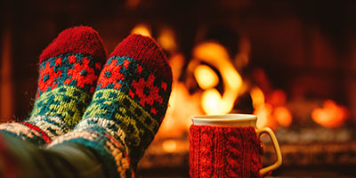 Coffee Cup and Feet in Winter Socks Sitting on Table in Front of Fireplace