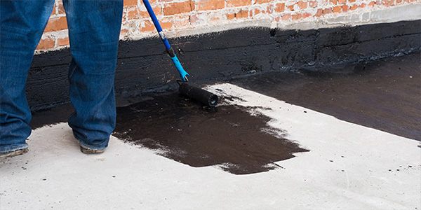 Person Applying Waterproof Sealant to Basement Wall and Concrete Floor