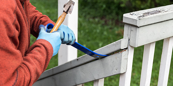 Person Lifting Up Deck Railing With Hammer and Pry Bar