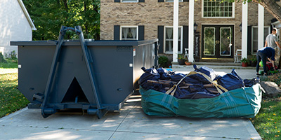 Blue Dumpster and Green Dumpster Bag in Driveway