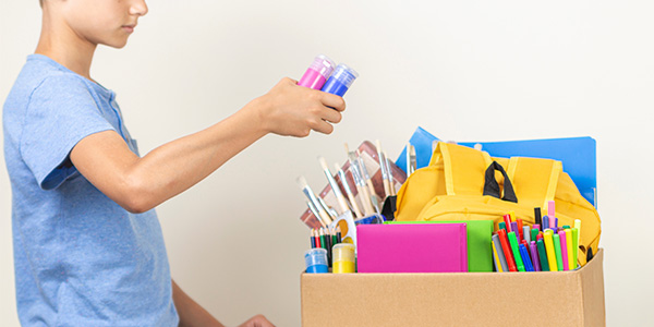 Child Placing School Supplies in Donation Box.