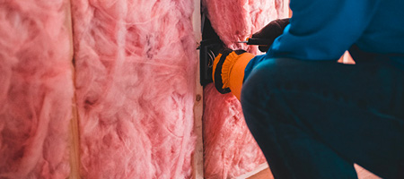 Person Using Staple Gun to Secure Attic Wall Insulation.