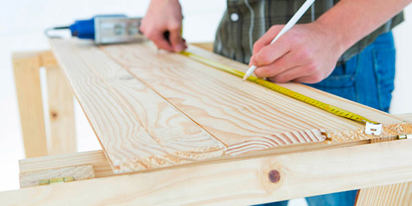 Man Measuring a Plank of Wood With a Tape Measure and Pencil.