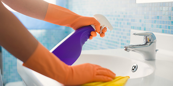 Gloved Hands Spraying and Wiping Down Bathroom Sink