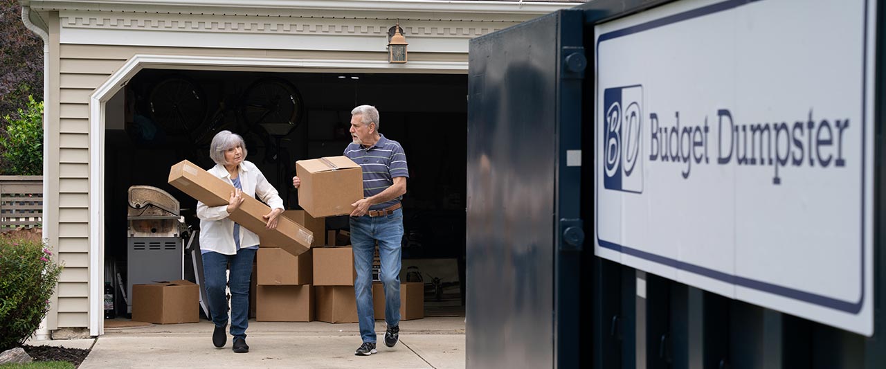 Couple Loading Boxes Into Dumpster