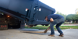 Person Placing Wood Under Roll Off Dumpster