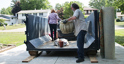 Couple Loads Household Junk Into Dumpster Through Open Door