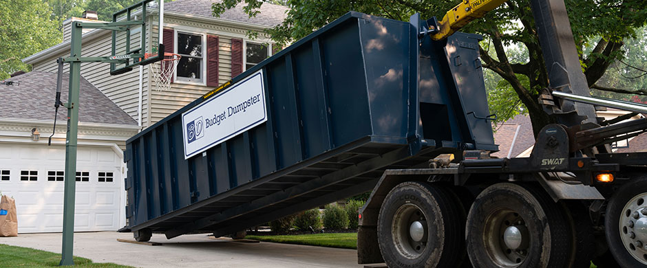 Truck Placing Blue Roll Off Dumpster On a Driveway