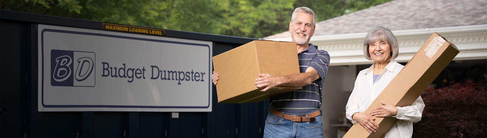 Couple Holding Boxes in Front of a Blue Budget Dumpster