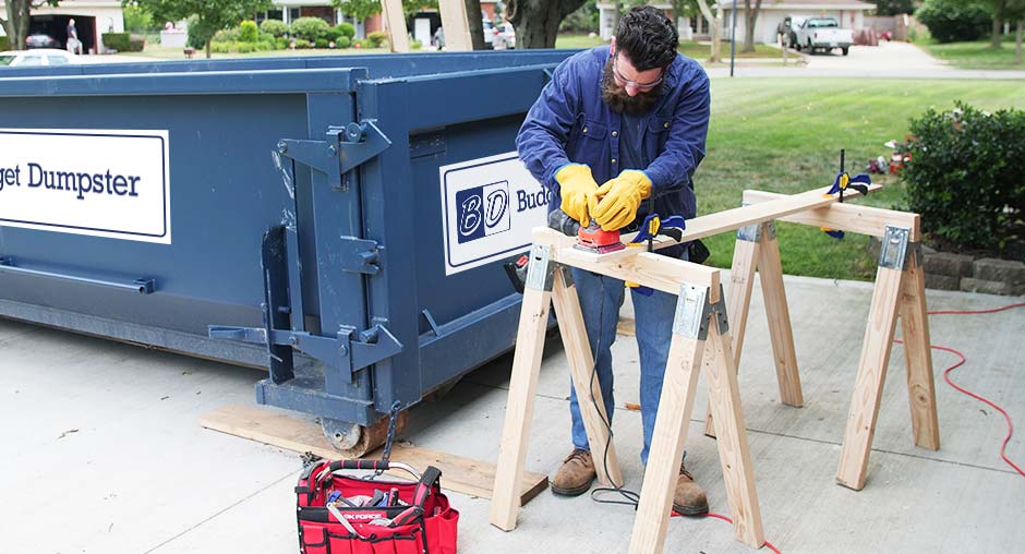 Man Working on Project Next to Blue Dumpster