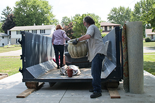 Workers Load Heavy Objects Into Dumpster Through Door