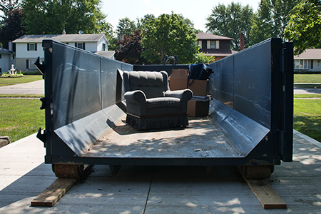 Couch and Boxes Sitting Inside Dumpster
