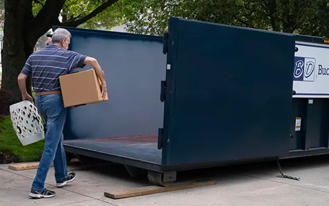 Man Carrying Household Junk Into a Dumpster