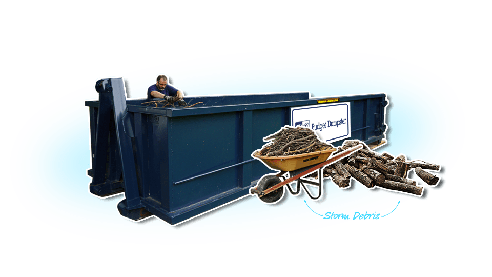 Man Filling Dumpster With Storm Debris With a Pile of Logs and Wheelbarrow of Sticks in Front