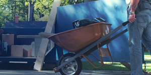 Man Walking Wheelbarrow Into Dumpster